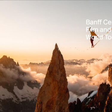 Person walking on tight rope above the clouds in the mountains as the sun sets.