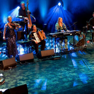 Band on stage playing a range of instruments under blue lights